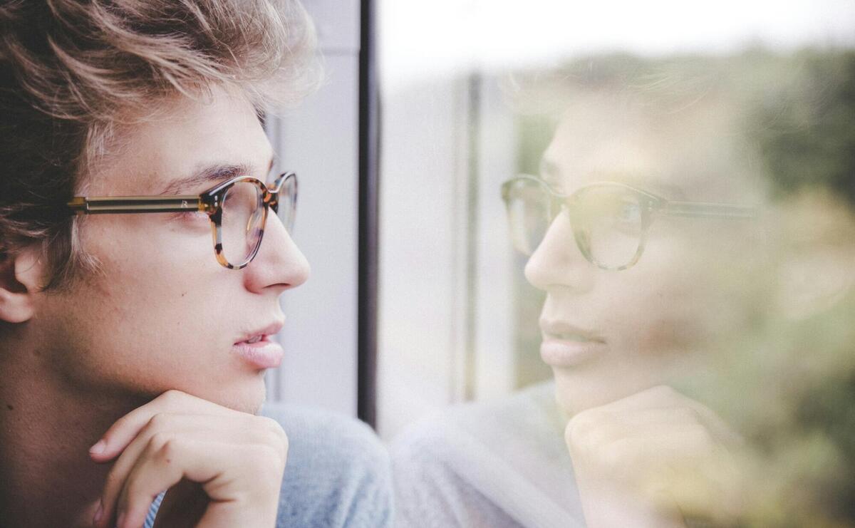 a man wearing glasses looking out a window