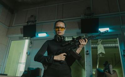 Confident woman wearing safety gear holding rifle at indoor shooting range.