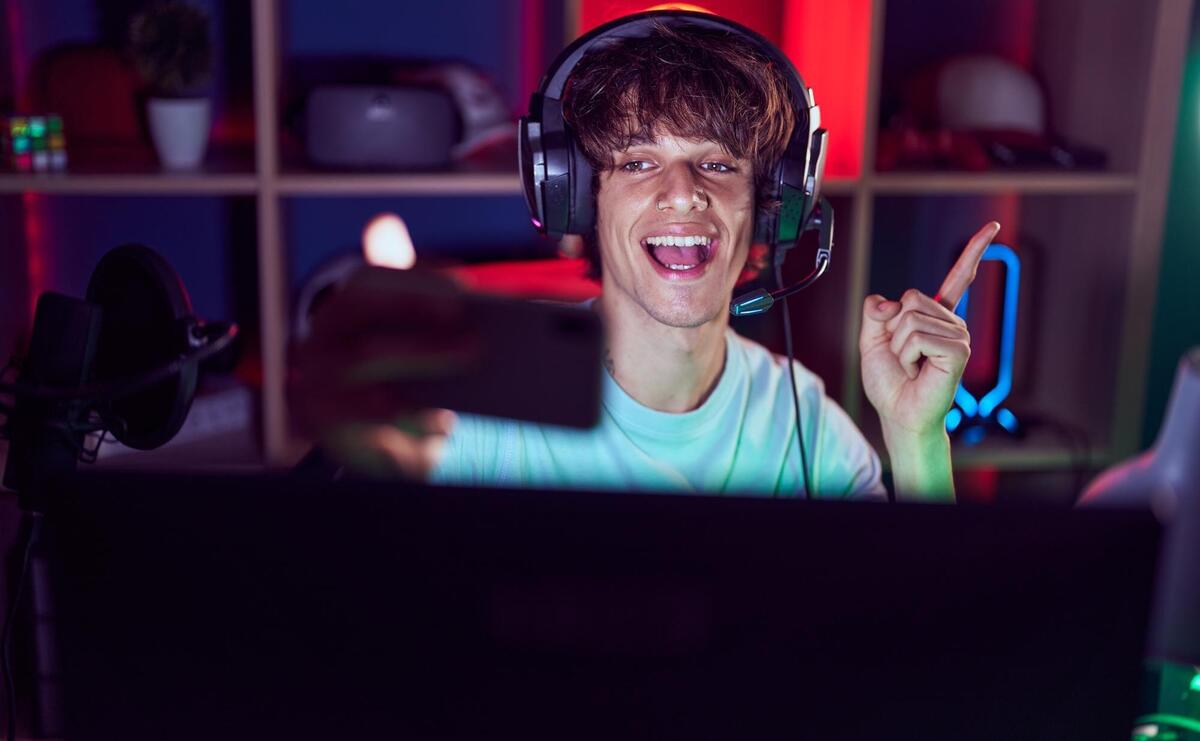 Hispanic young man playing video games with smartphone smiling happy pointing with hand and finger to the side