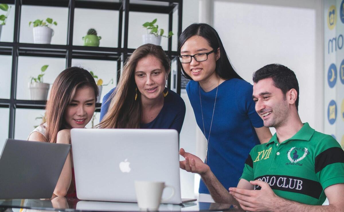 four people watching on white MacBook on top of glass-top table