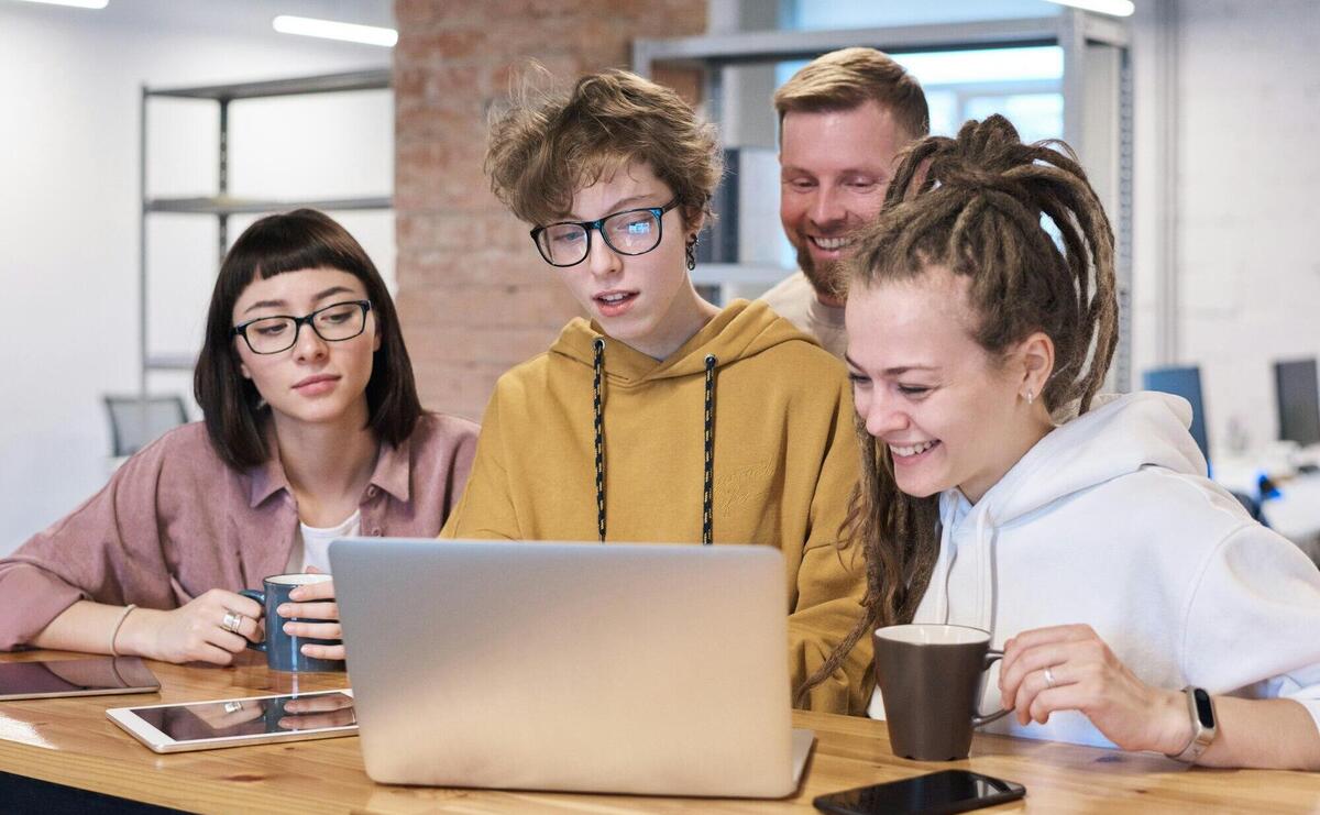 Young professionals in a vibrant office brainstorming on laptops and enjoying coffee.