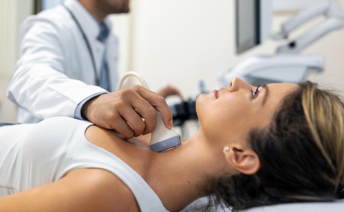 Close up shot of young woman getting her neck examined by doctor using ultrasound scanner at modern clinic