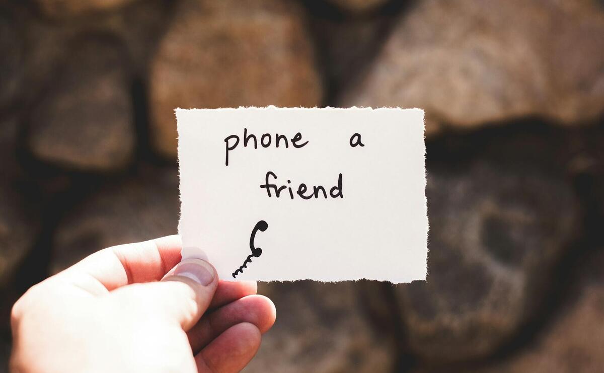 person holding piece of paper with phone a friend written text