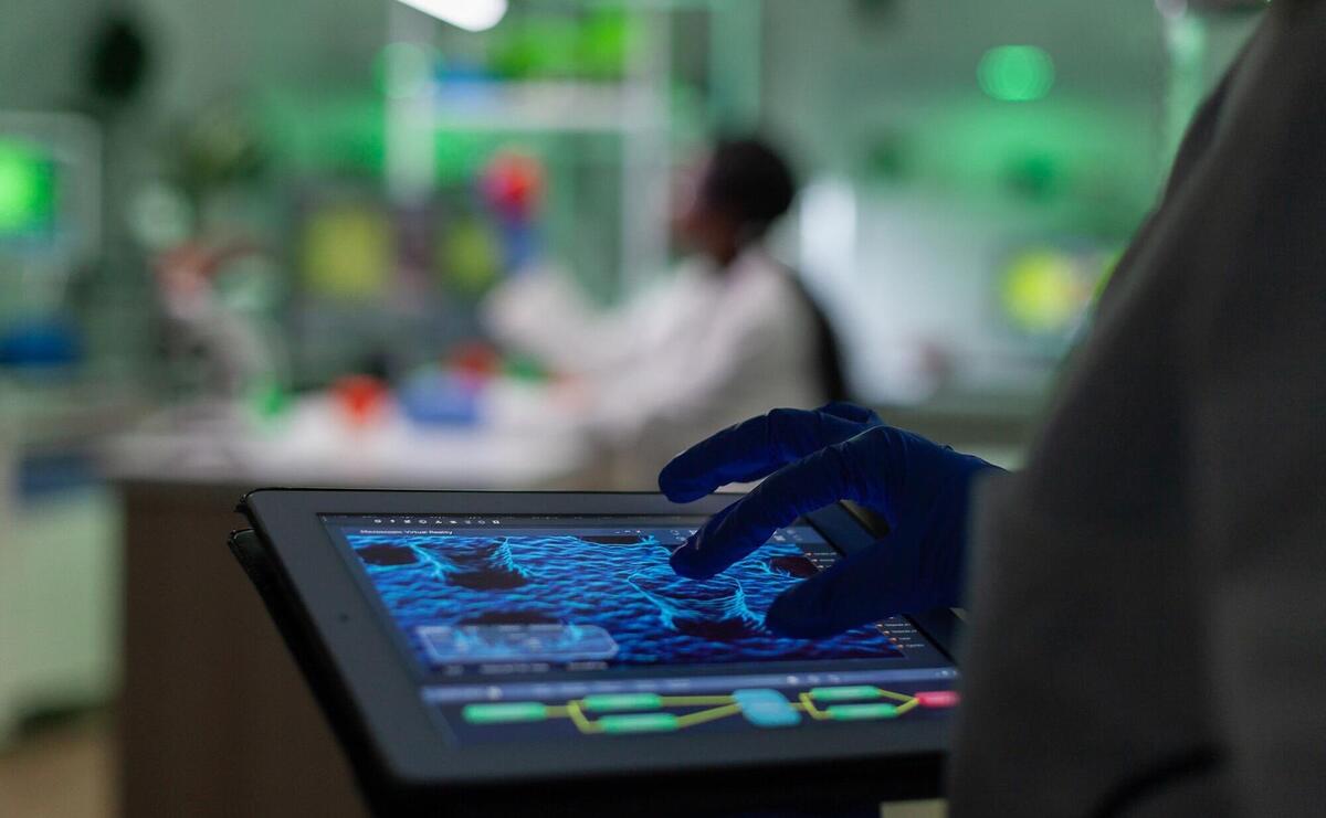 Scientist researcher doctor analyzing genetic mutation test using tablet while her collegue typing biological expertise on computer