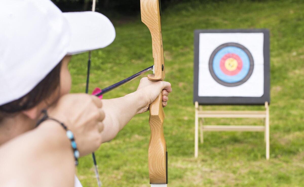 Young female archer holding his bow aiming at a target - sport and recreation concept