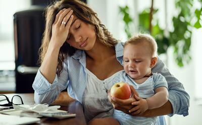 Young mother feeling exhausted while being with her baby and working at home