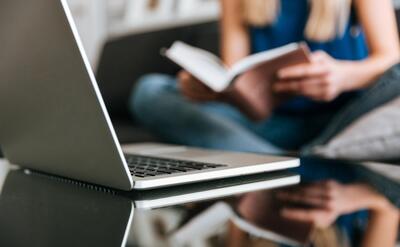 Laptop on the table near woman reading book at home