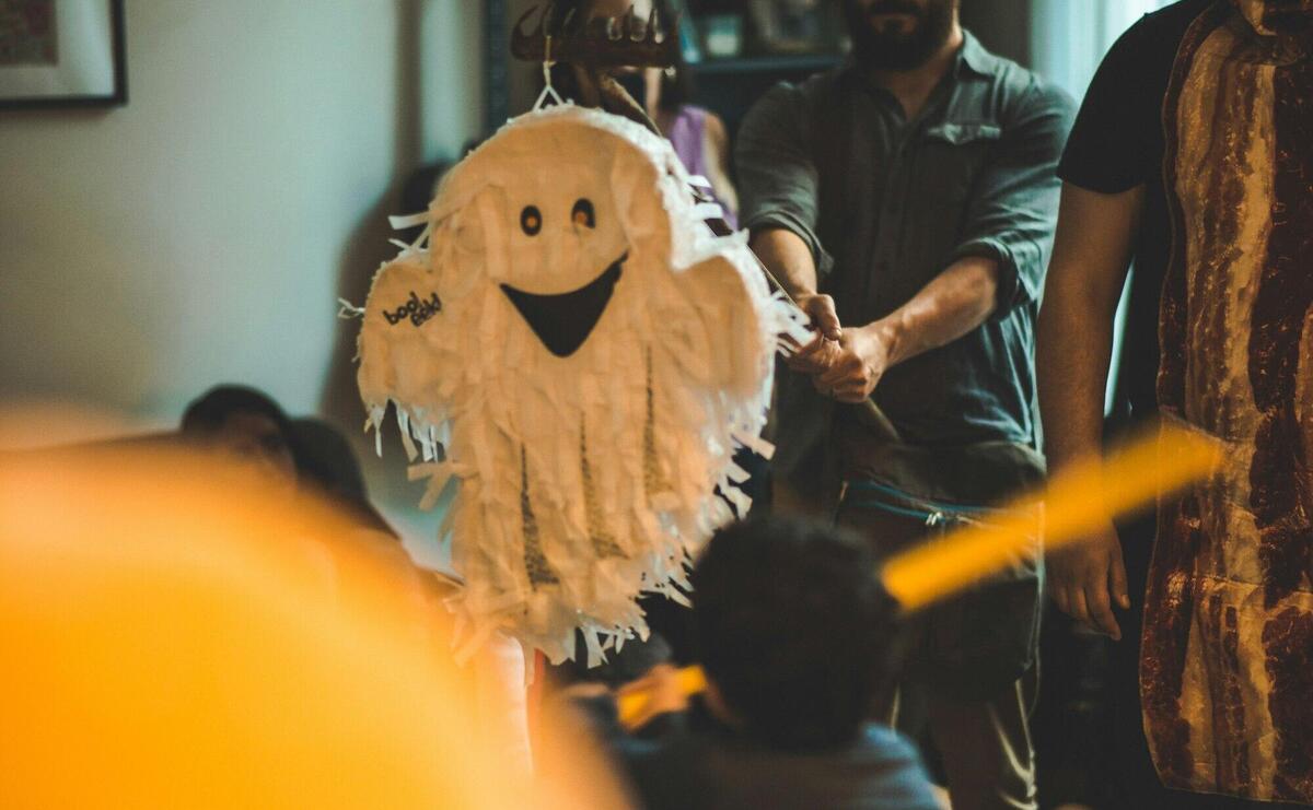 Person Holding Stick in Front of White Ghost Pinata