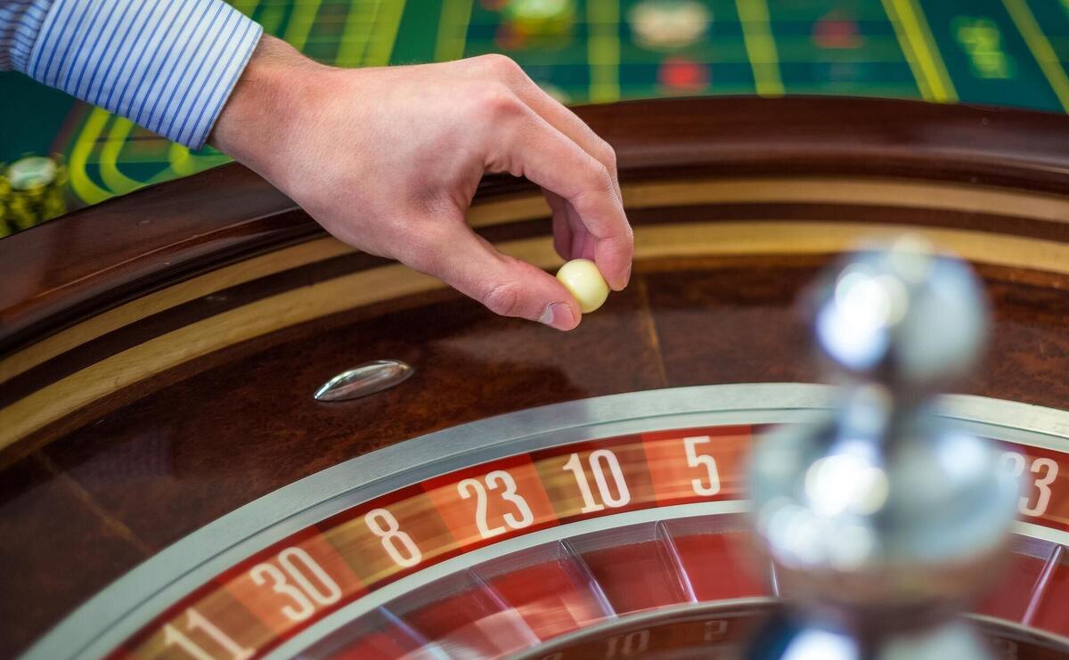 Roulette wheel and croupier hand with white ball in casino close up details