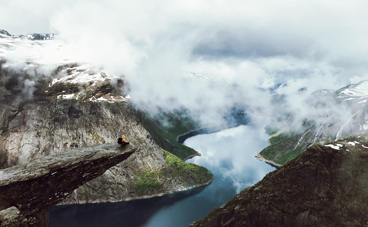 Man sits at the end of Trolltunga before the mountains