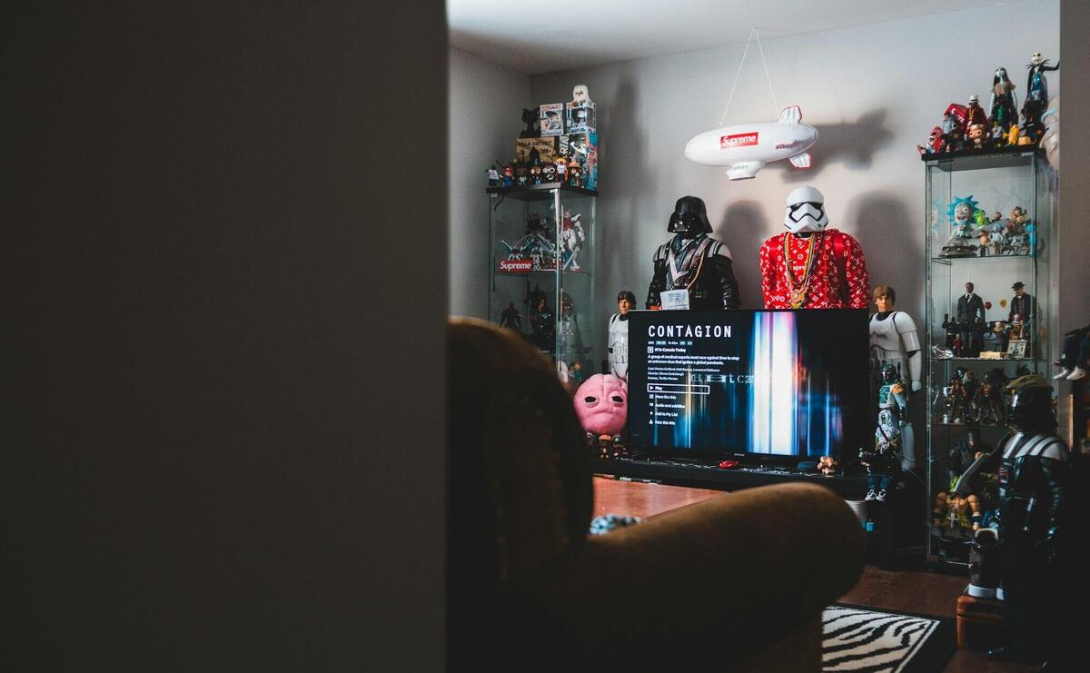 Interior of hipster style room with computer screen near glass shelves with assorted toy robots and hanging plane in front of cozy armchair with carpet on floor