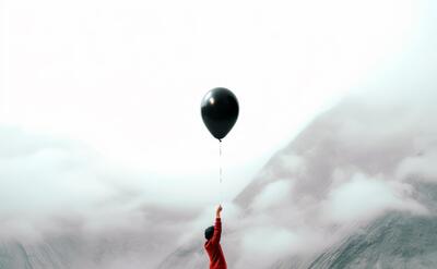 Person Holding a Black Balloon in Misty Landscape