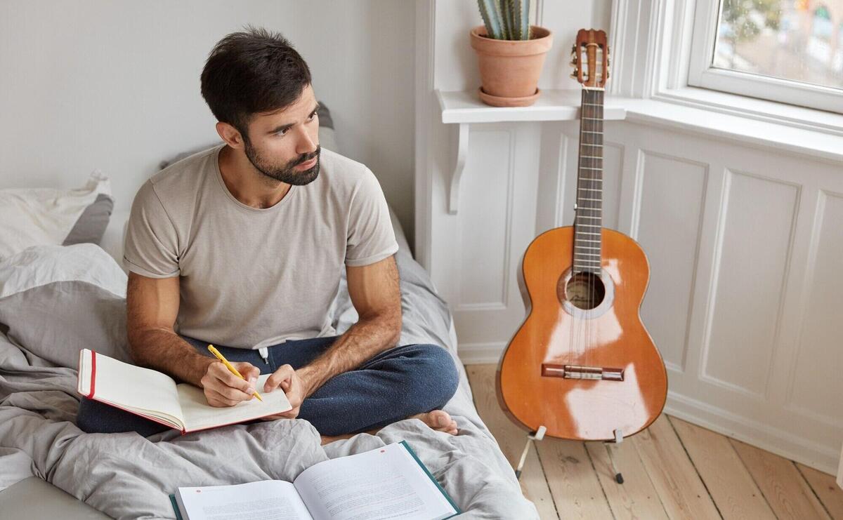 Pensive unshaven man sits in lotus pose on bed