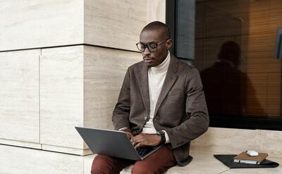 Stylish man in smart casual attire working on a laptop indoors with modern background.