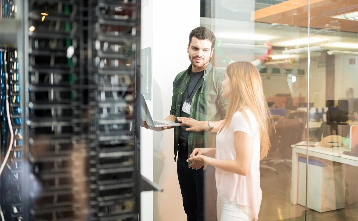 Two business people standing in server room with laptop and discussing