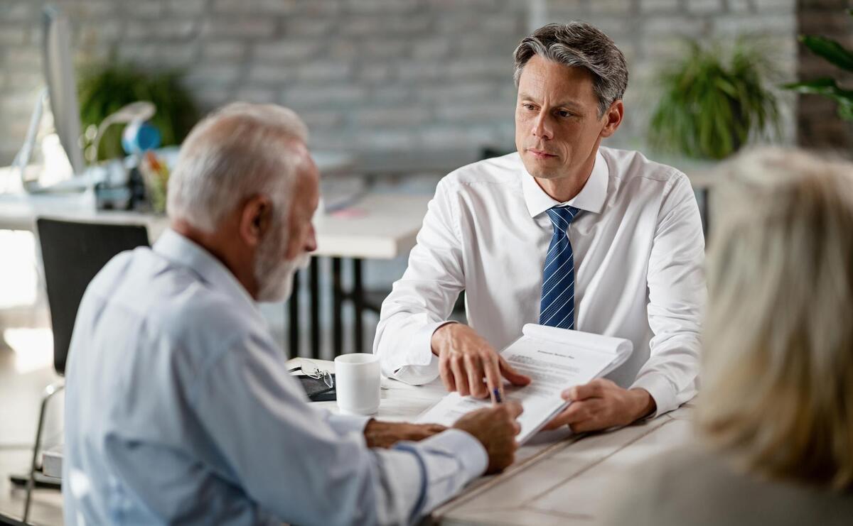 Insurance agent having a meeting with senior clients and pointing at place of the signature on a contract