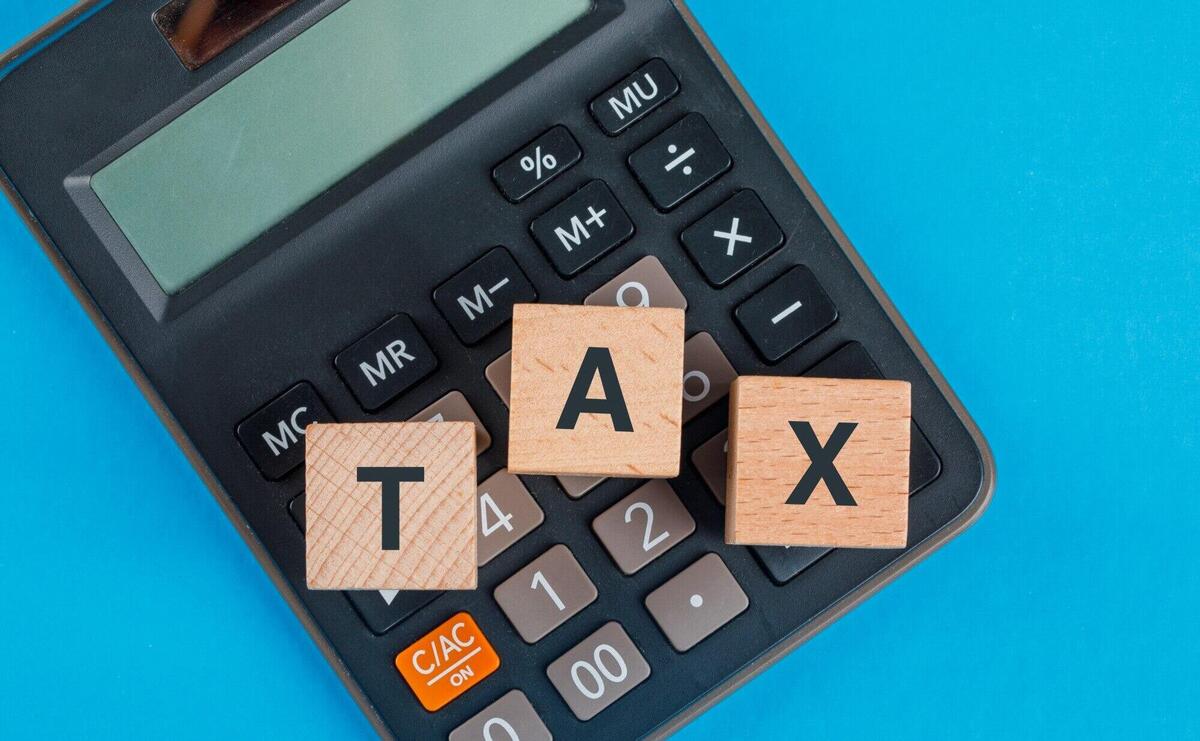 Tax planning concept with wooden cubes on calculator on blue table flat lay.