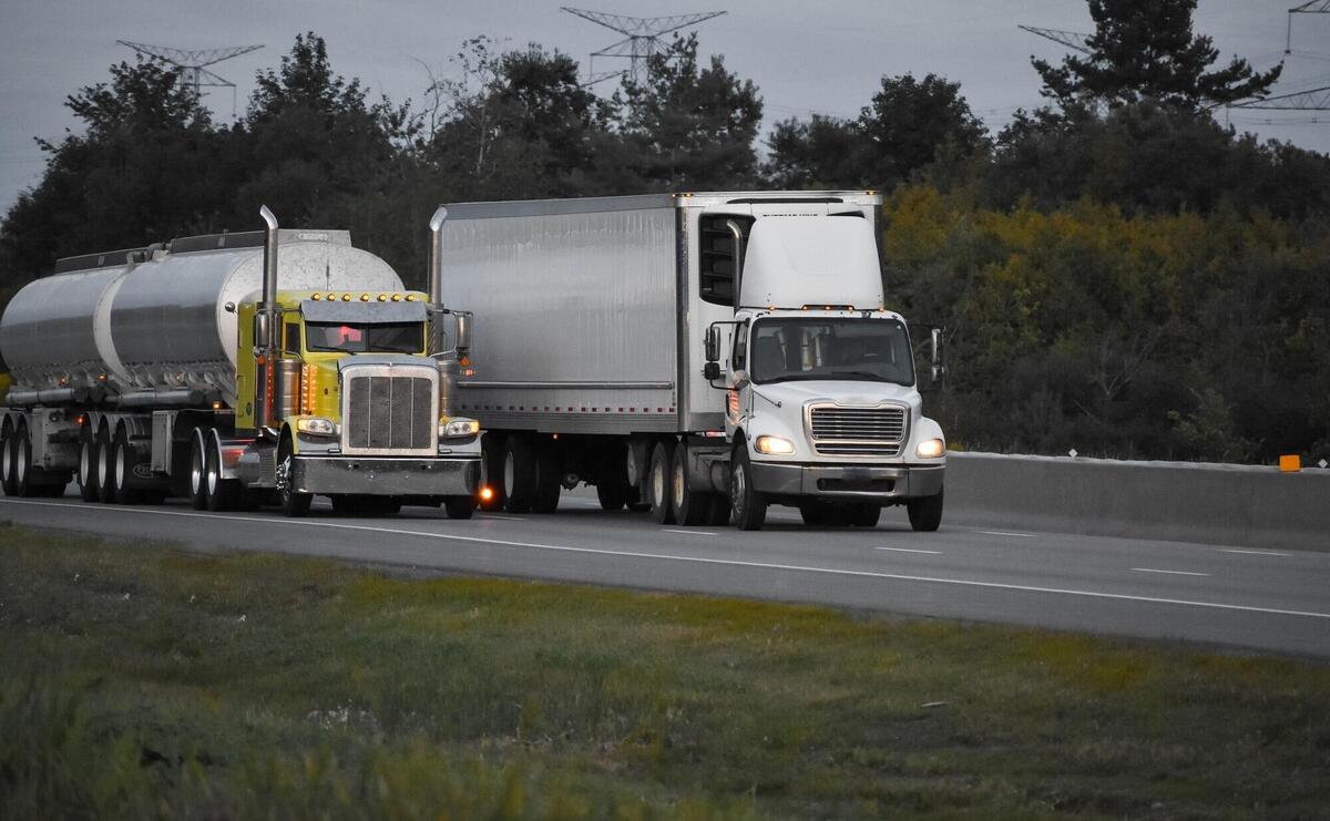 Trailer trucks driving on the road surrounded by beautiful green trees