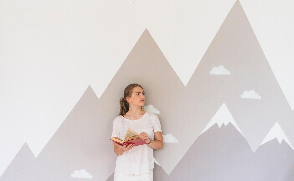 Young woman holding book standing against graffiti wall