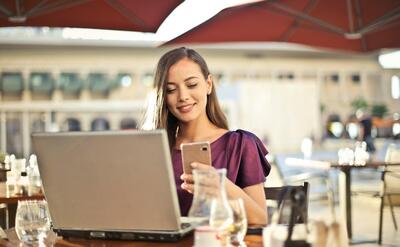 Woman enjoying remote work at a café, using a laptop and smartphone.