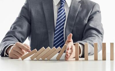 Businessman in a suit protecting wooden blocks from falling in a domino effect