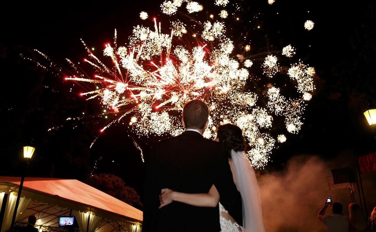 Happy hugging bride and groom watching beautiful colorful fireworks night sky