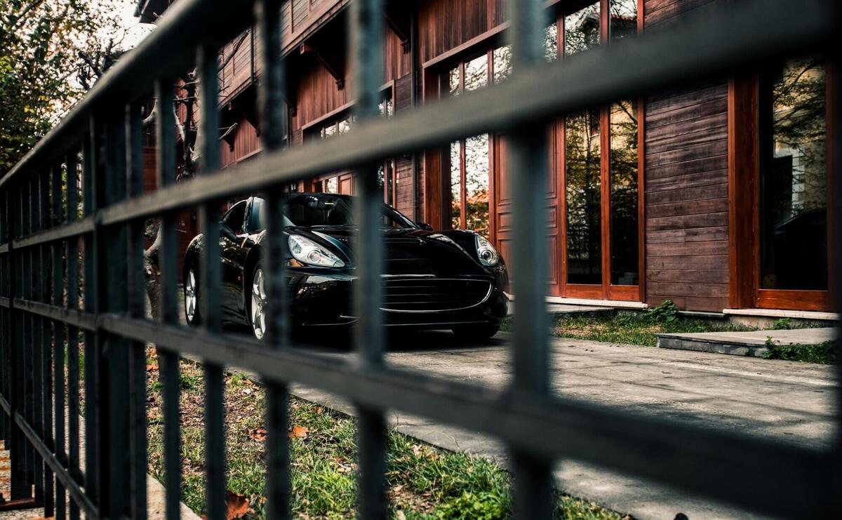 Sport sedan car, black color standing in front of a building, front view through a hence.