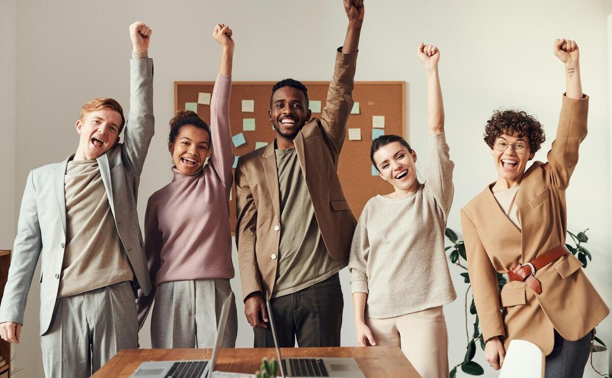 A diverse team celebrating success with raised hands in a modern office setting.