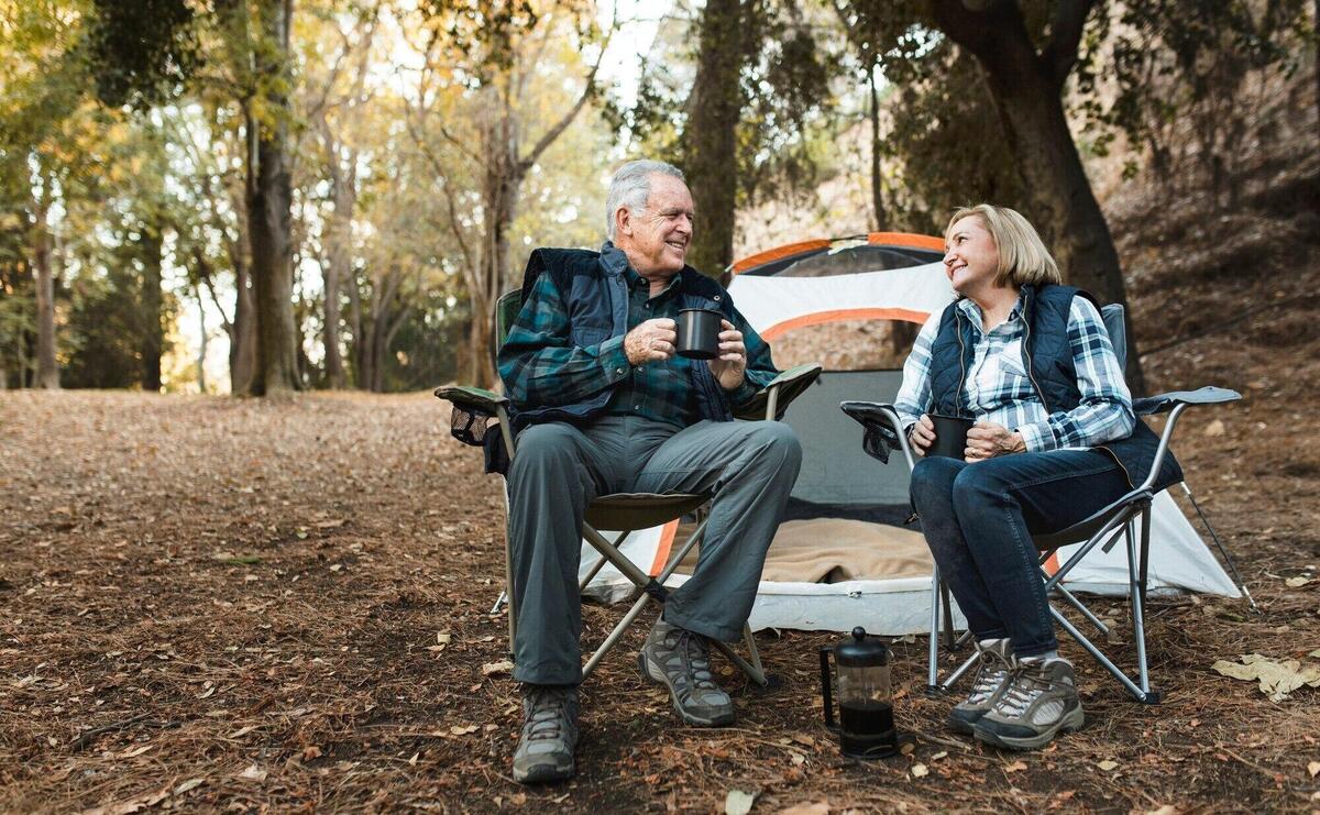 Happy retired couple having coffee by the tent in the forest