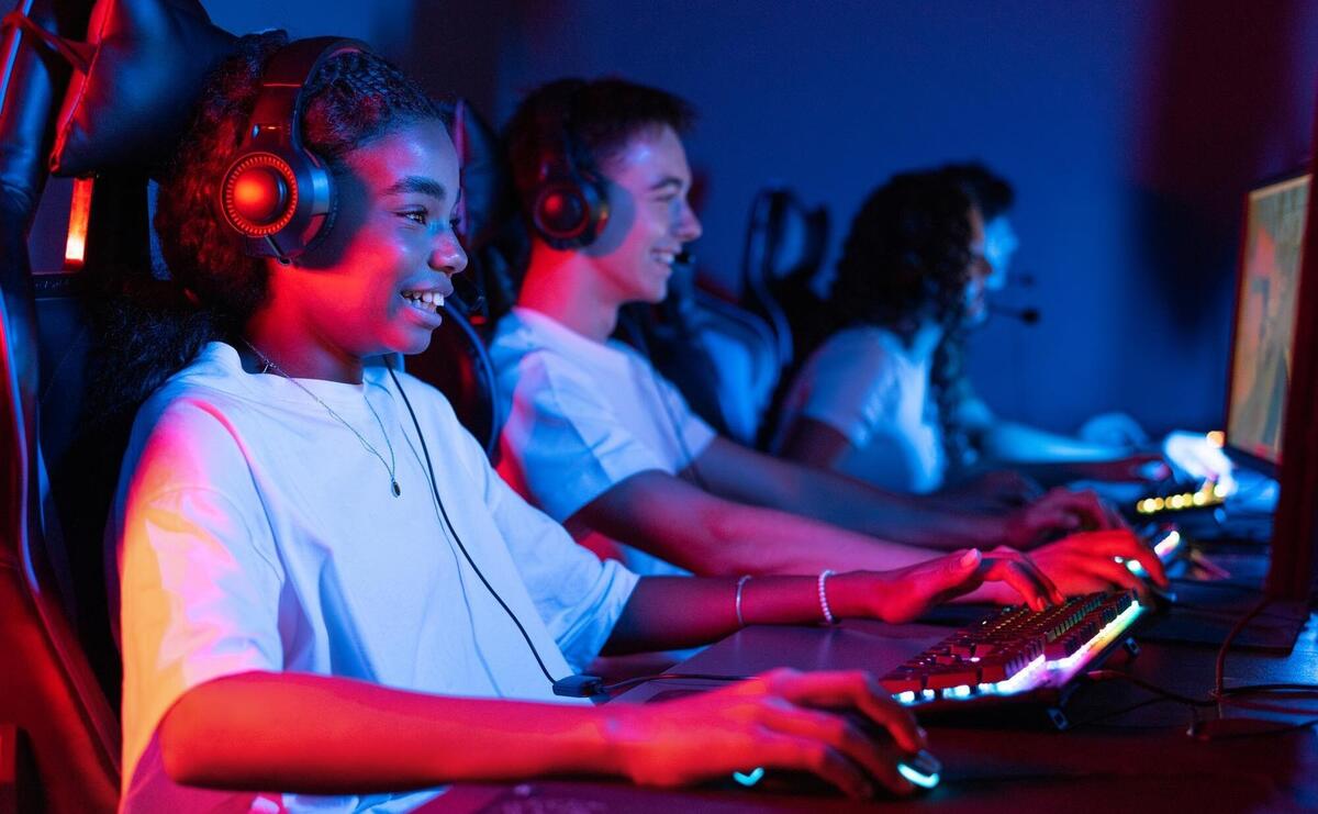 Group of multiracial teens in headsets playing video games in video game club with blue and red illumination Keyboard and mouse with illumination