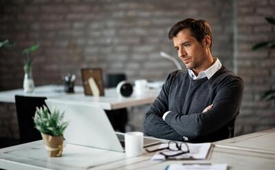 Displeased businessman with arms crossed reading an email on laptop at work