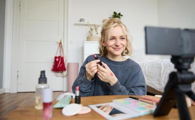 Portrait of young content maker woman blogger recording a video on digital camera showing lipstick