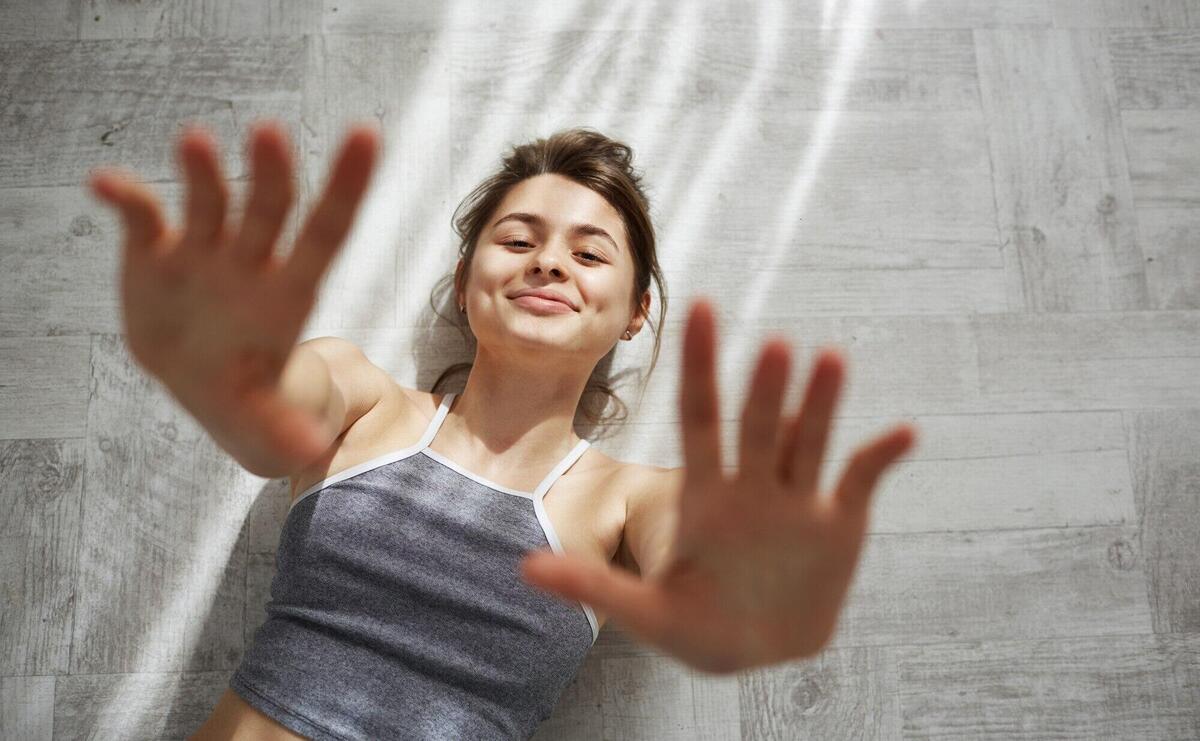 Portrait of young tender beautiful woman smiling stretching hands lying on floor in morning sunlights.