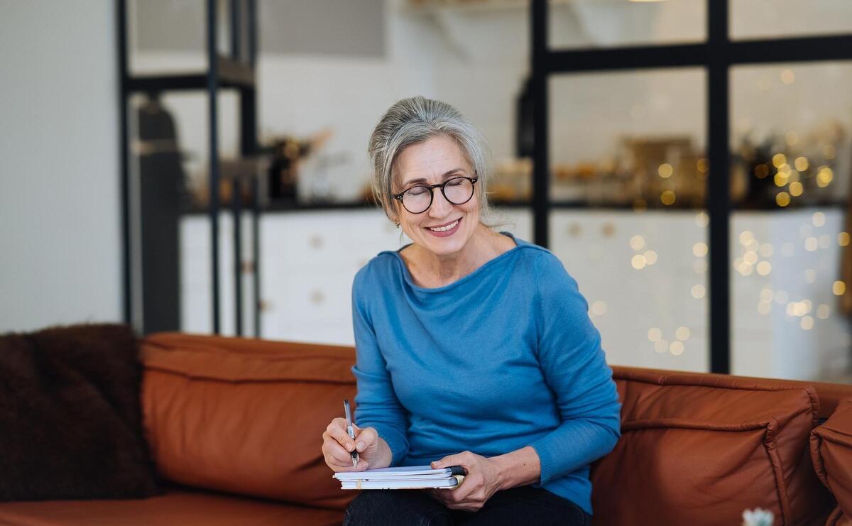 Happy senior woman in glasses writing to notebook or diary at home