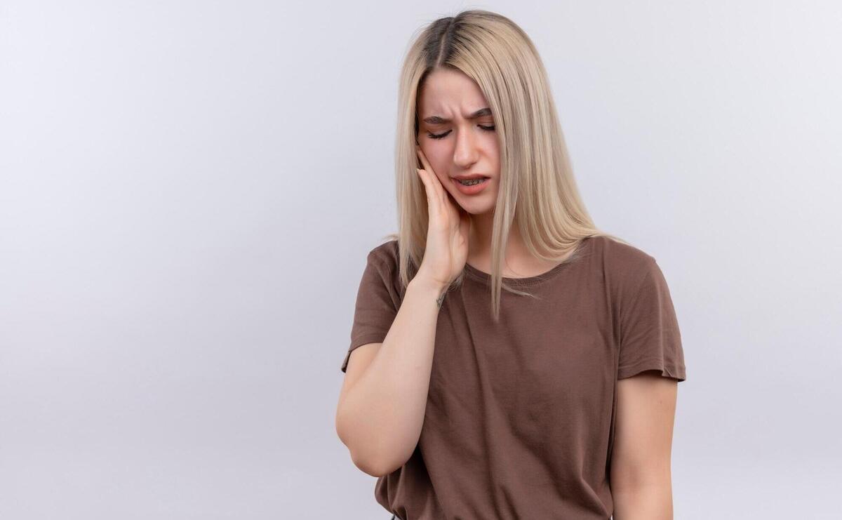 Aching young blonde girl putting hand on cheek having toothache on isolated white space with copy space