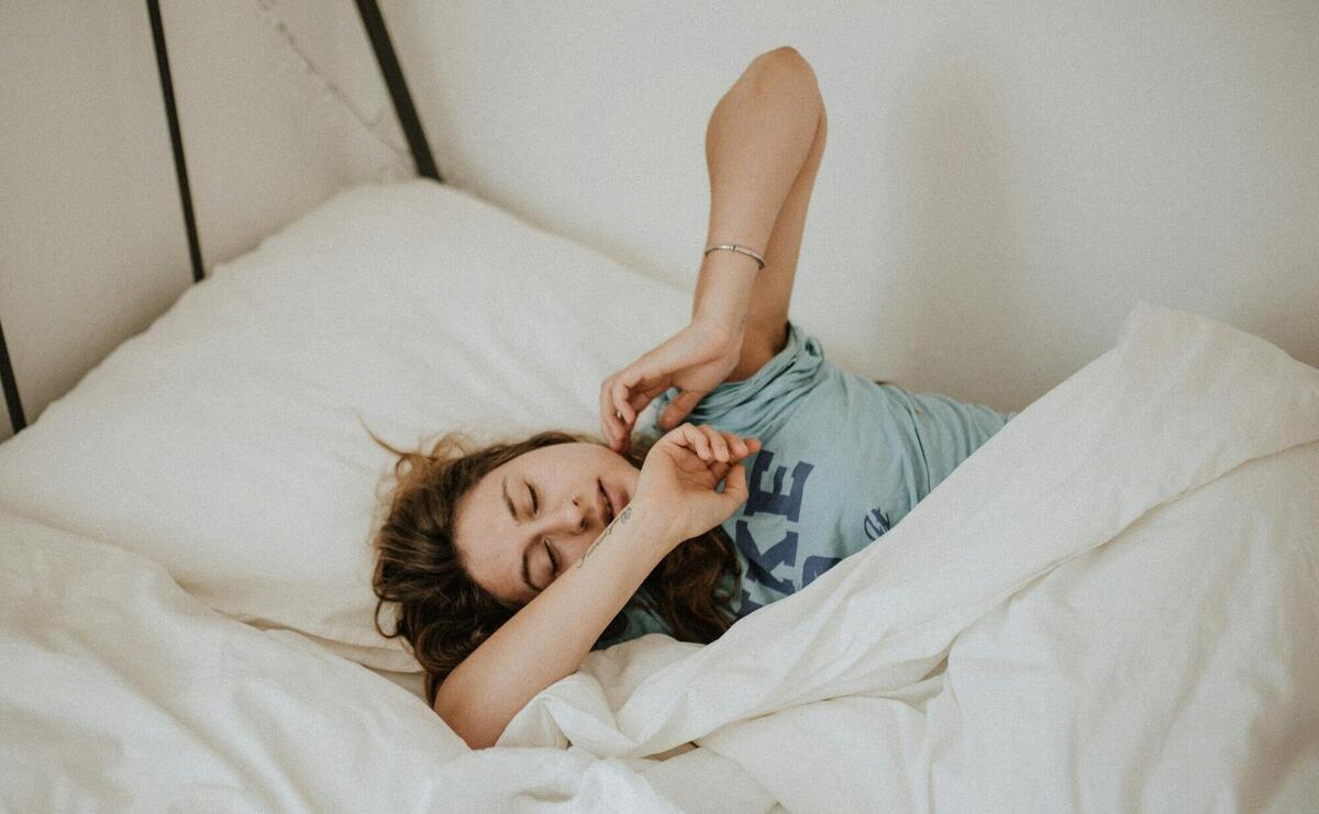 woman covered in white blanket sleeping on white bed comforter