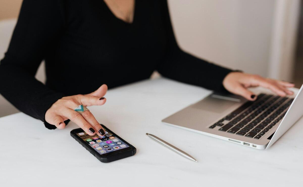 Crop woman using smartphone and laptop during work in office