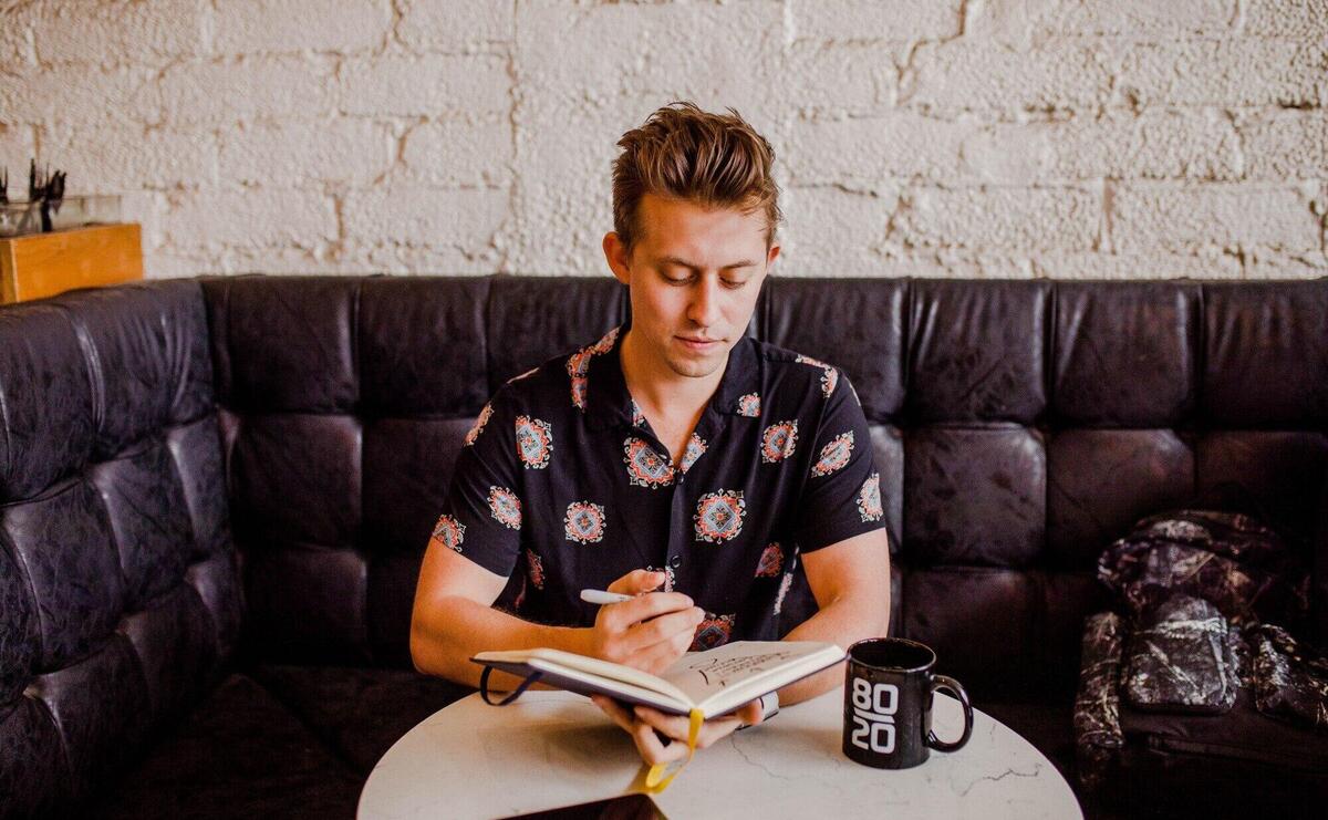 Boy sitting on a black sofa and taking notes in a notebook