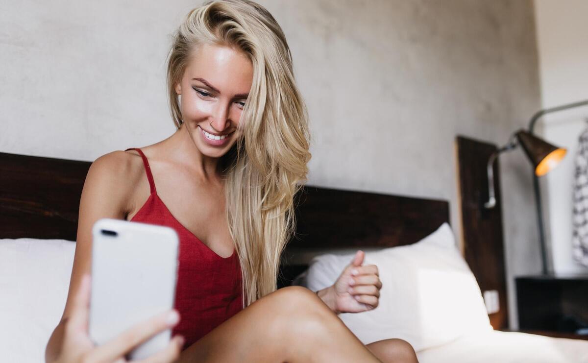 Carefree tanned caucasian woman using phone for selfie. Attractive laughing lady with tanned skin taking picture of herself.