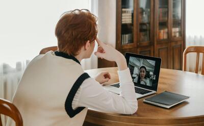 A man sitting at a table, using a laptop for a video call, set in a cozy indoor space.