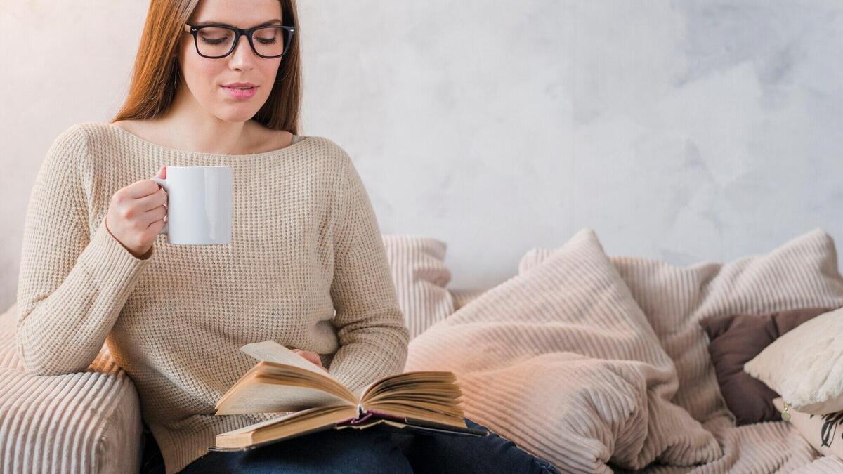 Panoramic view of young woman sitting on sofa reading book