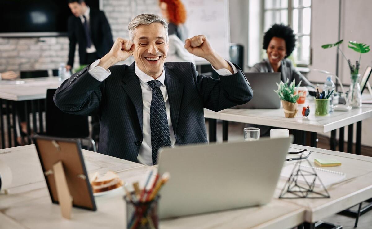 Happy businessman celebrating success while working on computer in the office