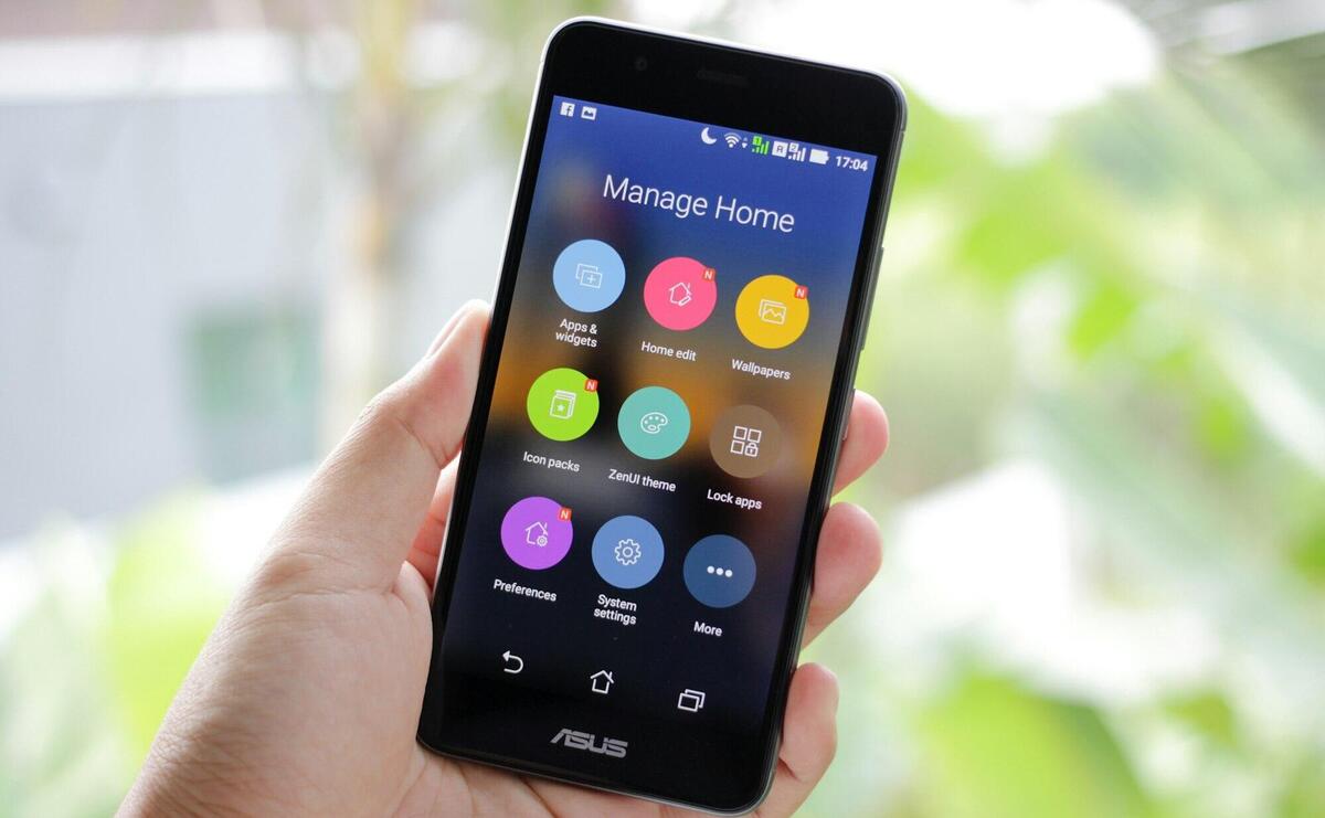 A hand holding a smartphone displaying home management apps on the screen.