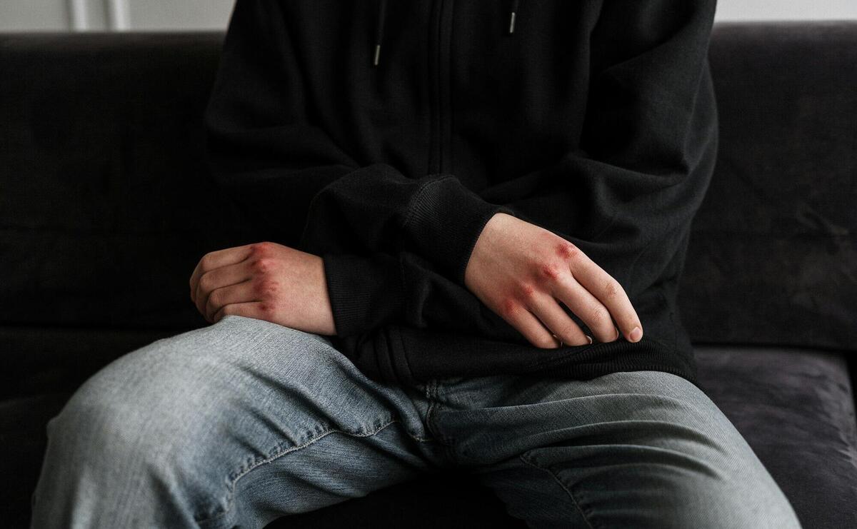 Person in Black Jacket and Blue Denim Jeans Sitting on Black Couch