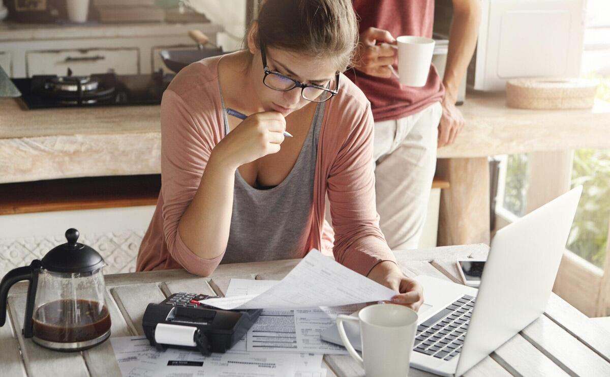 Attractive woman in spectacles having serious and concentrated look holding pen while filling in papers, calculating bills, cutting family expenses, trying to save money to make big purchase