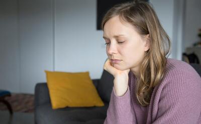 Upset young woman sitting on sofa at home, looking down