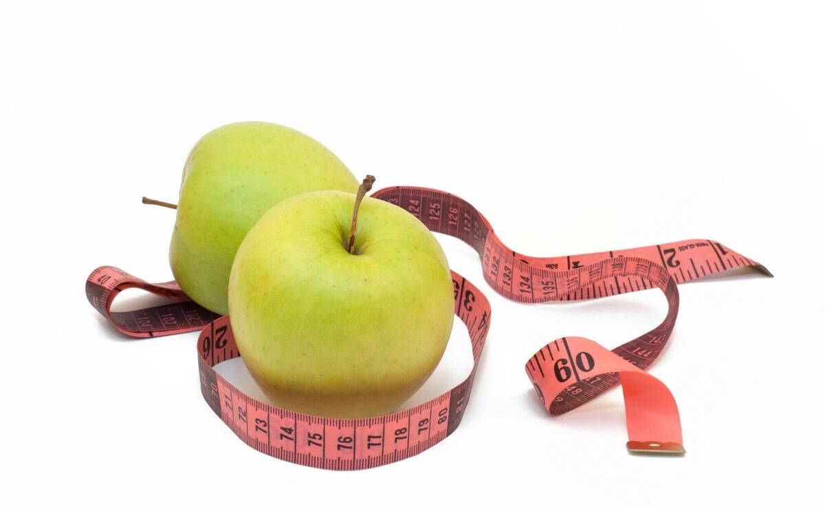 two green apples with a measuring tape around them