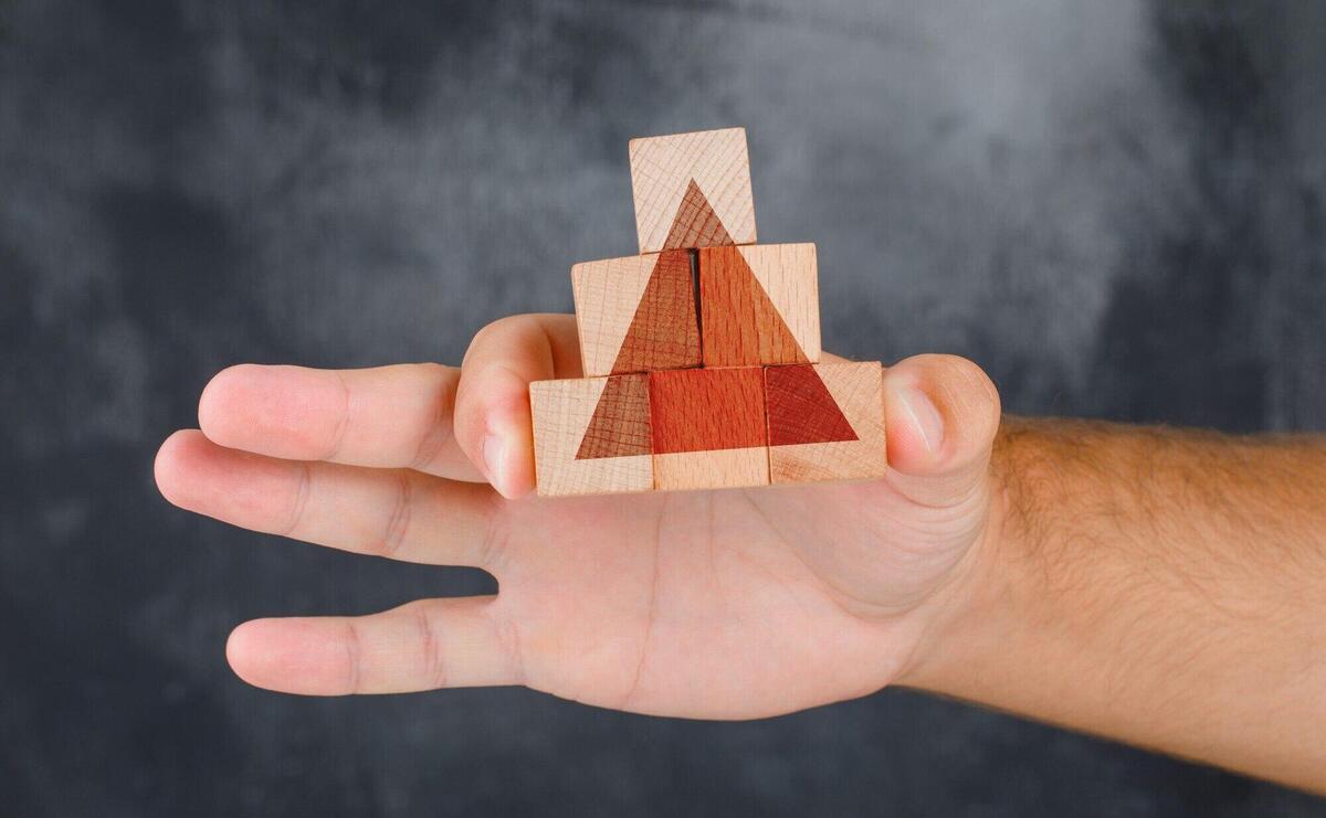 Business strategy concept side view. hand holding pyramid of wooden block.