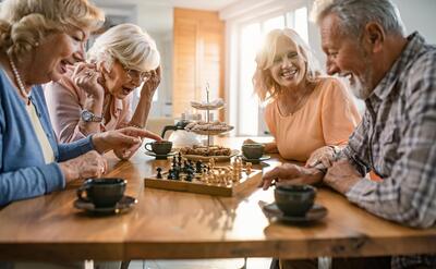 Group of happy seniors playing chess and having fun together at home